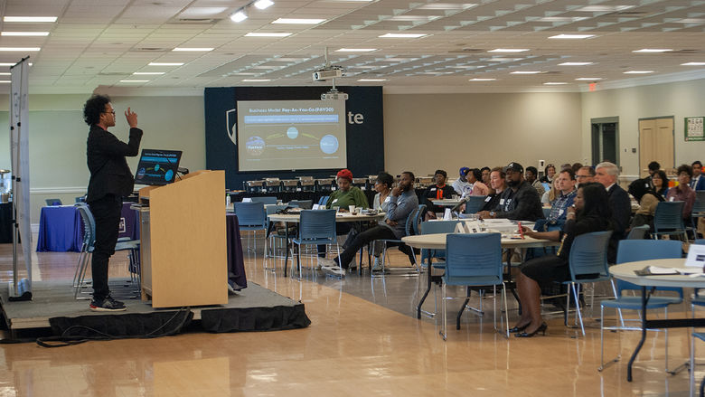 A student pitches a startup idea before a panel of judges and others