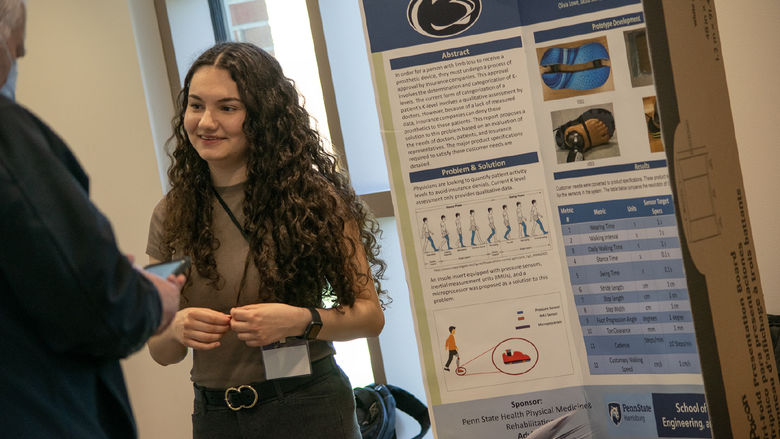 A student stands next to a research poster at the Capstone Design Conference