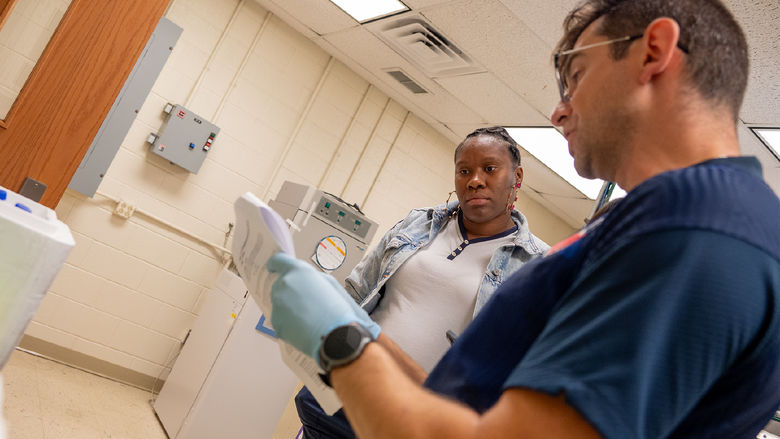 Two people stand in a lab, looking at a paper with instructions