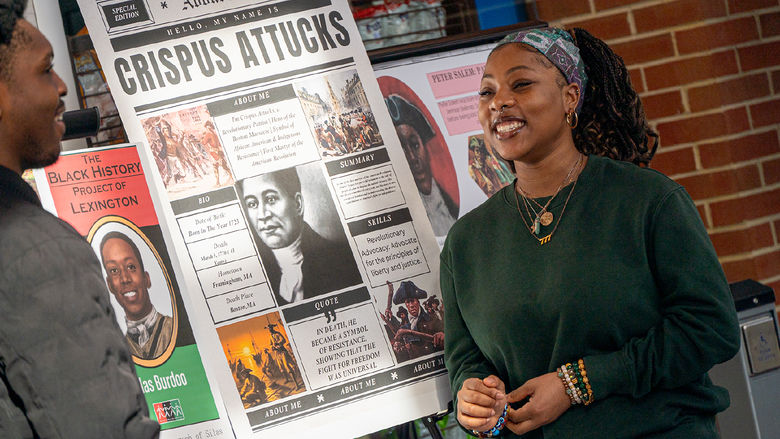 Students stand next to research posters and talk
