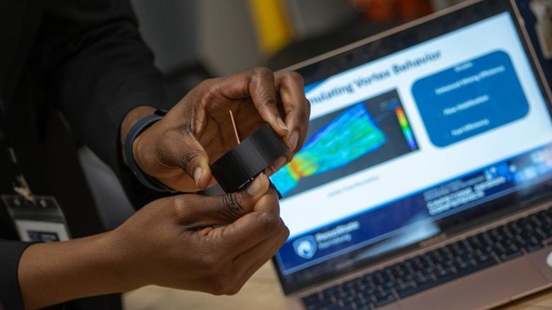 Closeup of a person's hands holding pieces of a science project, with a laptop in the background