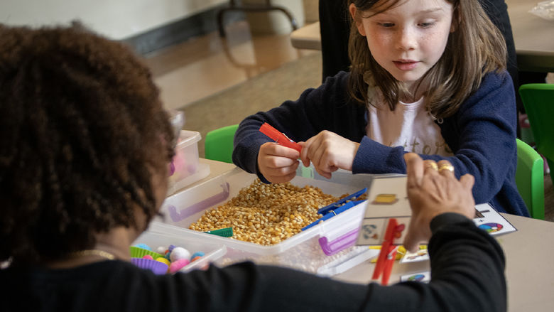 A child looks at symbols on a card, with a sensory bin in front of her