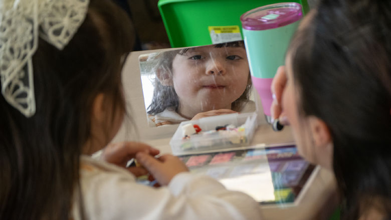 a child looks into a small mirror, lips pursed together