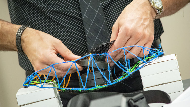 Closeup of hands placing weights onto a 3D printed bridge
