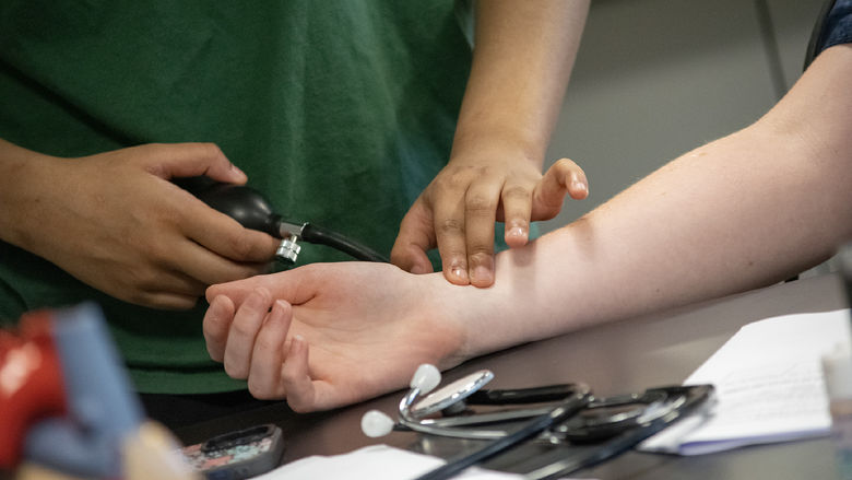 Closeup of a student checking another's pulse while taking blood pressure readings