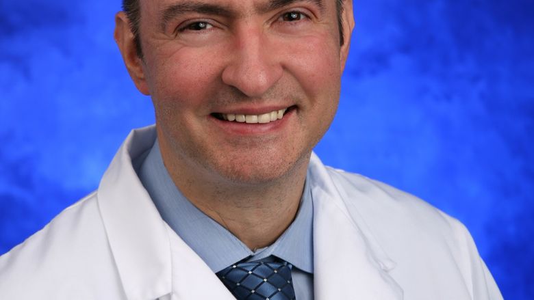 Dr. Sinisa Dovat smiles. He wears a white jacket with the Penn State Health Milton S. Hershey Medical Center and Penn State College of Medicine logo on the breast, a sport shirt and tie.