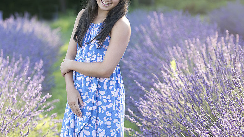 A young girl stands in a field and smiles for a photo.