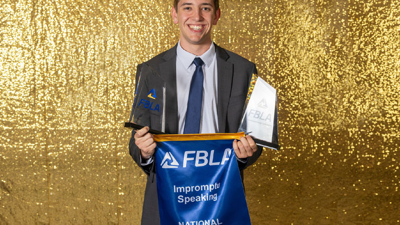 Aiden Beiler holds a flag that says FBLA National Champion Impromptu Speaking