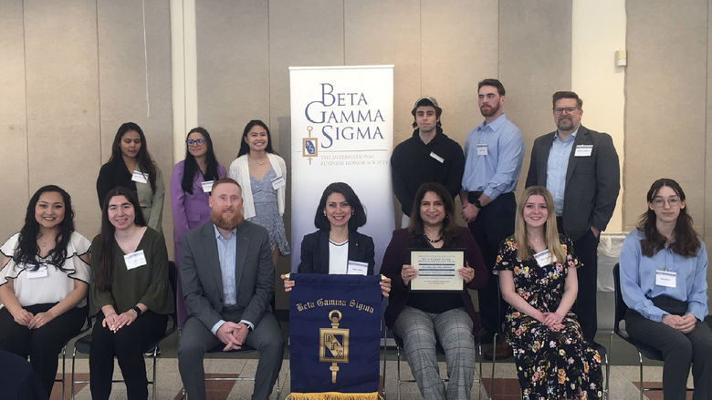 A group of people sitting and standing near a banner that says Beta Gamma Sigma