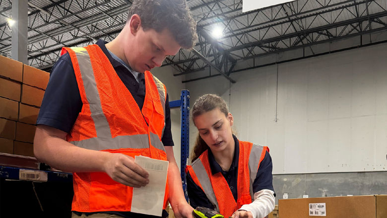 Two people in orange vests scan the barcode on a package in a workplace
