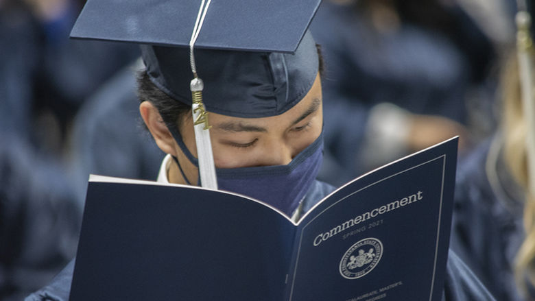graduate in cap and gown reading commencement program