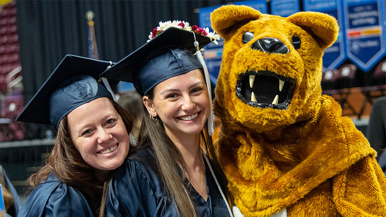 The Nittany Lion hugs two new graduates in caps and gowns