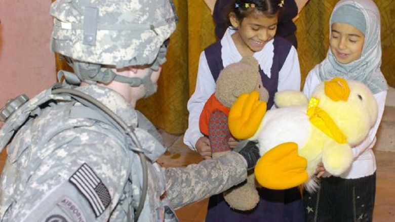 A man in an Army uniform hands stuffed animals to children