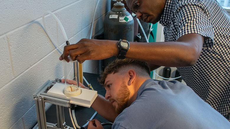 A student and a professor look at a device with tubes attached