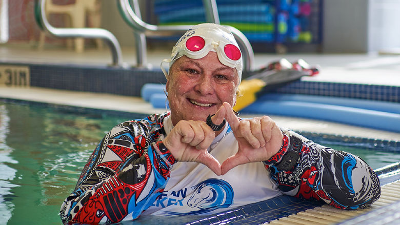 Holly Maitland-McKenna is shown in a swimming pool, smiling and making a diamond shape with her hands.