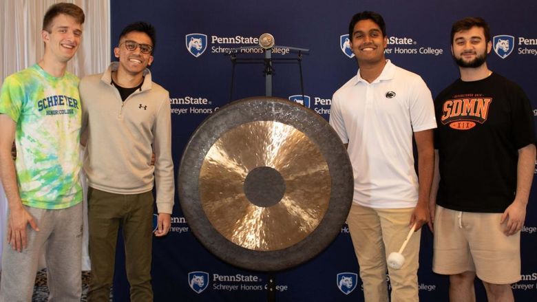 A group of 3 Schreyer Scholars pose with the gong