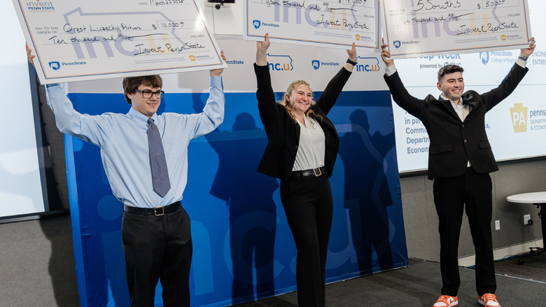 Three individuals stand on a stage holding up oversized checks