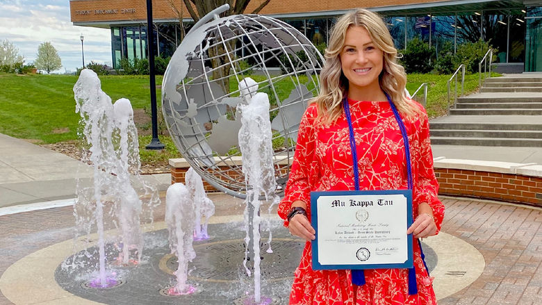 Kylee Altland in from of globe fountain holding certificate