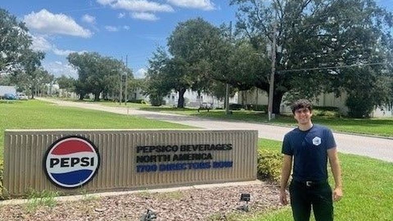 A student stands in front of a PepsiCo sign