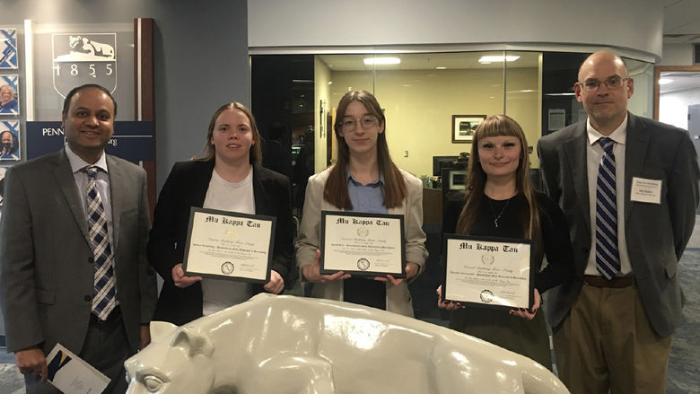 A group of people stand around the Nittany Lion statue in Olmsted Building. Three students hold certificates.