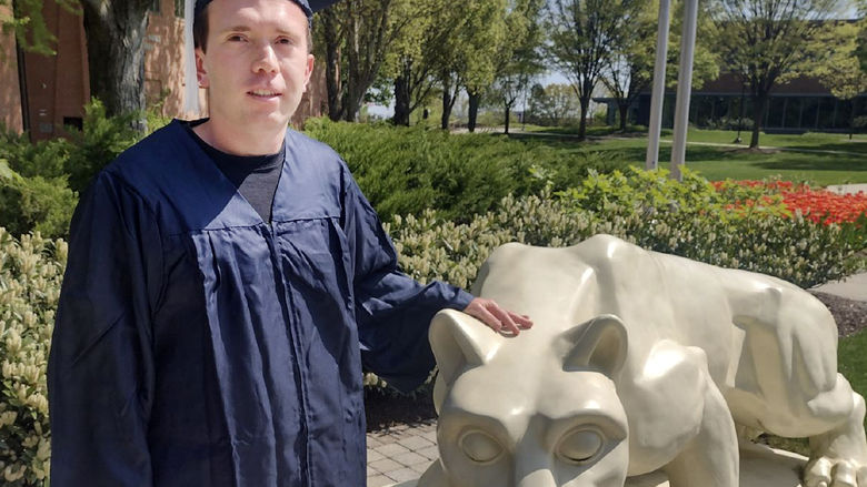 Nick Spohn in commencement regalia with Lion Shrine at Penn State Harrisburg