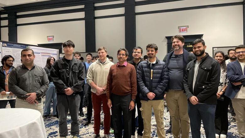 Penn State students and faculty stand in a line for a photo surrounded by their research posters during poster session.
