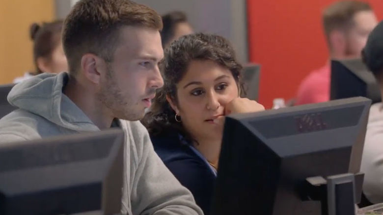 business students peer at a computer monitor in class