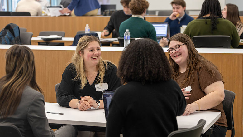 Four students sitting around a desk and laughing during Policy Simulation Competition