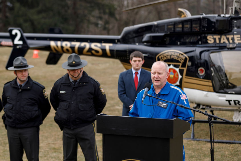 A man speaks at a podium in front of a helicopter