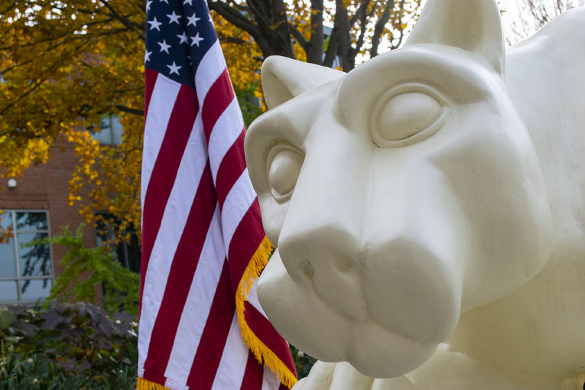 Photo of a U.S. flag next to the Nittany Lion statue 