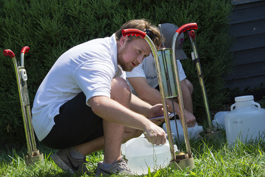 Two men pour water into a device planted in the ground to measure infiltration rates