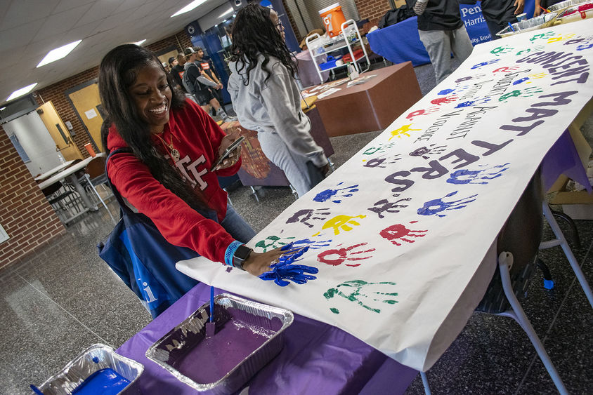 A student presses her hand, painted blue, on a banner with the words "Consent Matters."