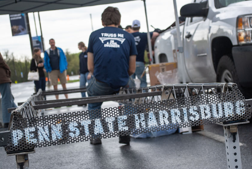 A student sits on the edge of a steel bridge that has "Penn State Harrisburg" painted on it