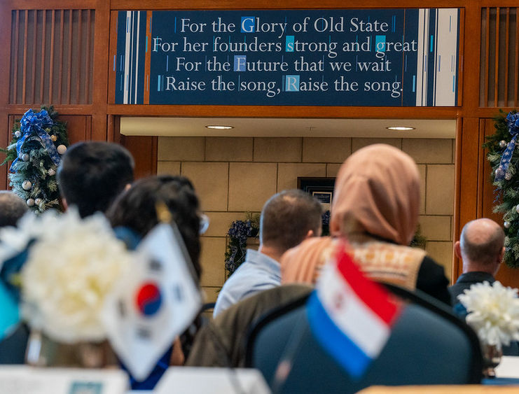 Two table flags in the foreground with a plaque of Penn State's Alma Mater in the background