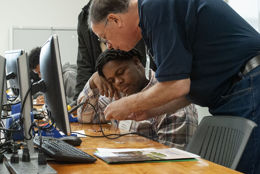 A Penn State Harrisburg faculty member helps a high school student with an activity, in front of computer monitors