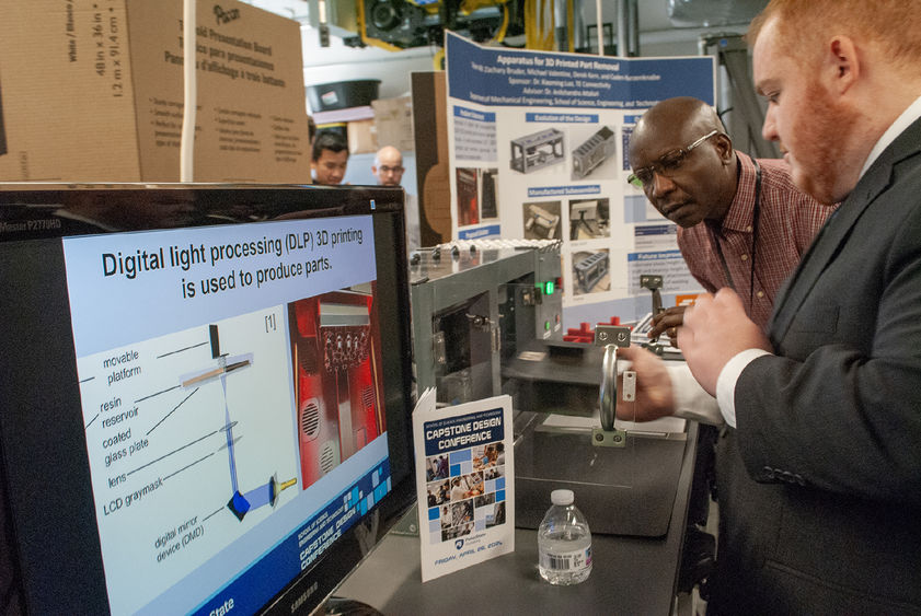 A student talks to a faculty member in front of a capstone project