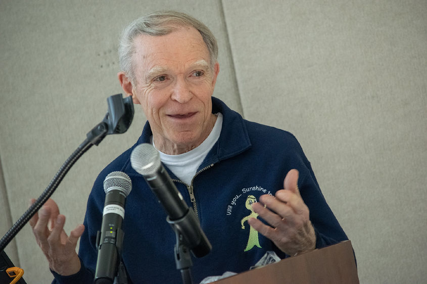A man speaks at a podium from behind microphones