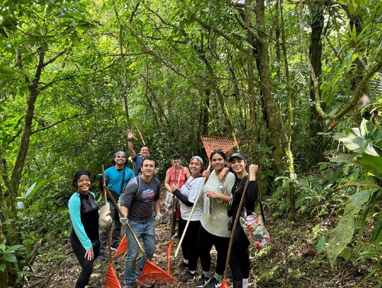 Group of students hold rakes while standing in the rainforest