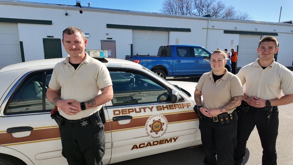 Three people standing in front of a deputy sheriff academy vehicle