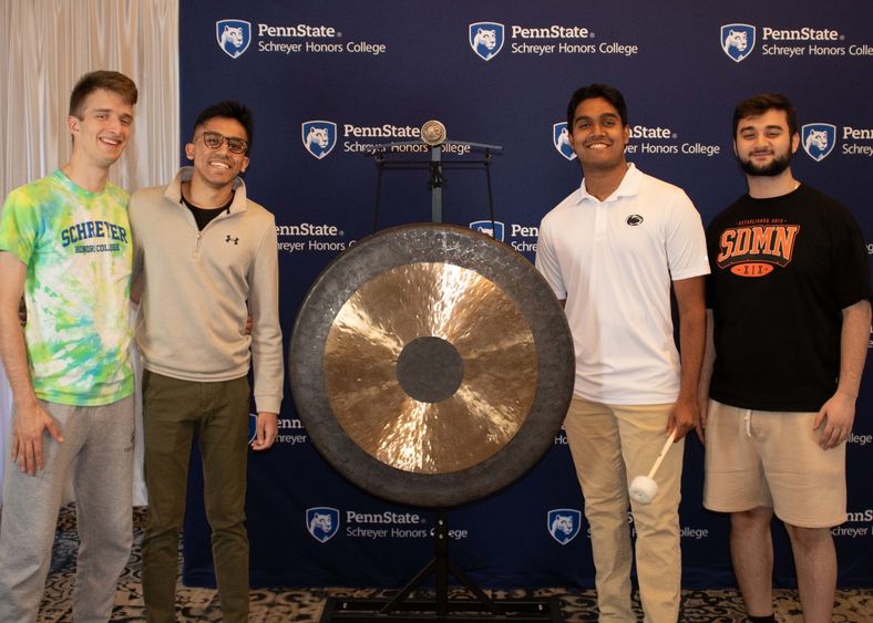 A group of 3 Schreyer Scholars pose with the gong