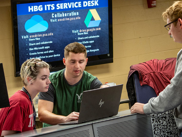 Student workers at the ITS Service desk look at someone's laptop.