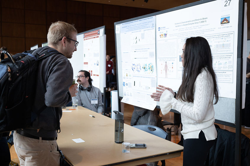 student in front of poster presenting research to male