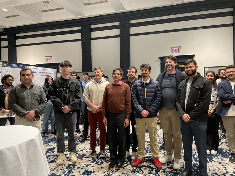 Penn State students and faculty stand in a line for a photo surrounded by their research posters during poster session.
