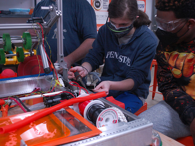 Two people wearing masks use soldering equipment. 