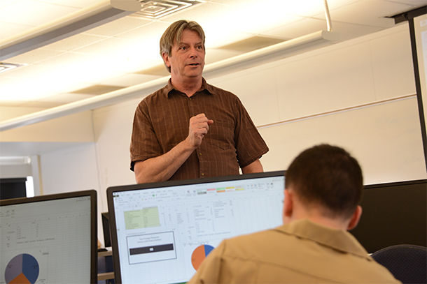 A standing person talks to a person sitting down at a computer. 