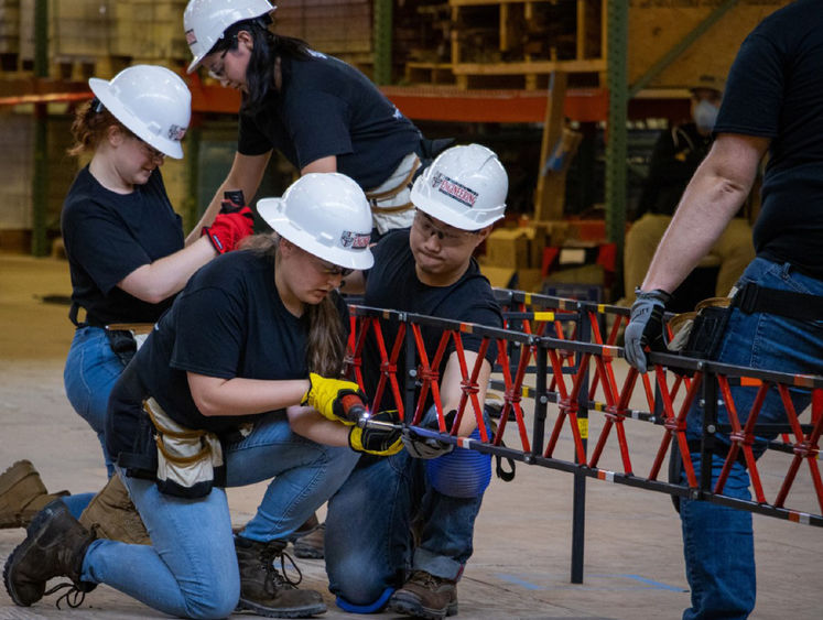Students wearing hard hats and too belts work to construct a steel bridge during a previous ASCE event.